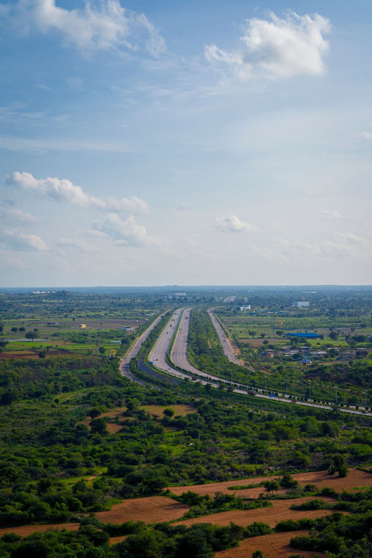 Vista aérea de uma rodovia de pista dupla atravessando uma região de campos e vegetação.
